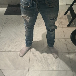 Blå slitna jeans från dondup - Säljer ett par blå jeans med slitningar på låren och knäna. De har en slim passform och är perfekta för en avslappnad stil. Jeansen har klassisk femficksdesign och stängs med dragkedja och knapp. Modellen är 185. Pris kan diskuteras vid snabb affär!