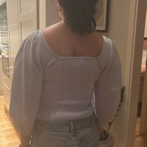 Ljusblå blus med puffärmar - Säljer en stilren vit blus med puffiga trekvartsärmar och en fyrkantig urringning. Blusen har en åtsittande passform med sömmar som ger en korsettliknande look. Perfekt för att lyfta vilken outfit som helst!
