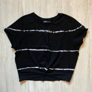 Svart och vit randig t-shirt New Yorker - Cool svart t-shirt från FB Sister med vita horisontella ränder i batikstil. T-shirten har korta ärmar och en twistad detalj framtill. Perfekt för en avslappnad stil.