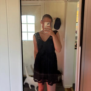 Svart spetsklänning med v-ringning - Säljer en svart kortklänning med v-ringning och spetsdetaljer både fram och bak. Klänningen är ärmlös och har en lätt utställd kjol. Perfekt för dig som vill ha en stilren och feminin look. Dragkedjan bak går ända upp