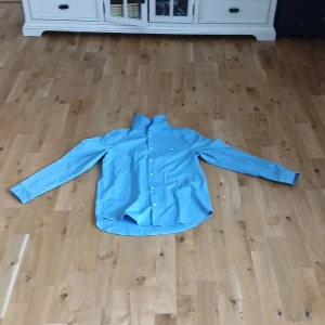 Blå prickig skjorta från L.O.G.G. - Säljer en ljusblå skjorta från L.O.G.G. med små vita prickar och broderad logga på bröstet. Skjortan har klassisk krage, knäppning framtill och långa ärmar. Perfekt för dig som gillar stilrena detaljer!