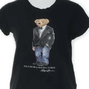 Svart t-shirt med Polo Bear från Ralph Lauren - Svart t-shirt från Ralph Lauren med ikoniska Polo Bear-motivet på bröstet. Björnen är klädd i smoking och jeans. Klassisk rund hals och korta ärmar. Perfekt för dig som gillar streetstyle och vill ha något unikt.