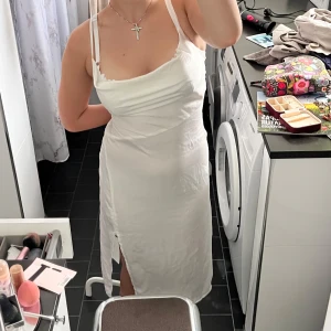 Vit långklänning med slits och smala axelband - Säljer min gamla studentklänning, köpt på sellpy men bara använts en gång på studenten. Jag hqr sytt om den i brösten så den passar mig som vanligtvis brukar ha S perfekt, tror att jag köpte sen som en M men den är ju som sagt insydd.