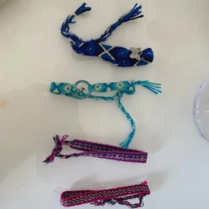 Färgglada vänskapsarmband i tyg - Fyra handgjorda vänskapsarmband i olika färger och mönster. Ett blått med silverfärgad blomdetalj, ett turkost med drömfångare, ett lila och ett rosa med vävt mönster. Perfekta som accessoar för att ge din stil en personlig touch.