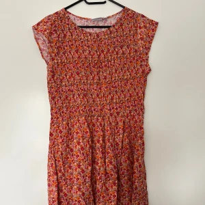 Blommig klänning, Saint Tropez, S - Färgglad klänning med blommigt mönster från Saint Tropez. Storlek S. Klänningen har ett smockparti över bysten. Klänningen är i nyskick.  100% viskos.   Mått: Längd ca 92 cm Byst ca 42 cm Midja ca 42 cm Ärmlängd ca 8 cm Axelmått ca 34 cm