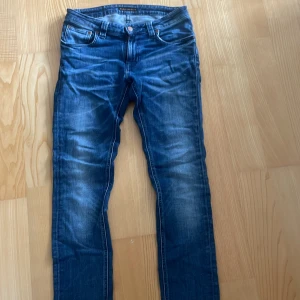 Nudie jeans - Säljer ett par klassiska blå nudie jeans med snygg tvätt och raka ben. Jeansen har dragkedja och knapp med logga. Perfekta för dig som gillar en tidlös och enkel men ändå skön stil.