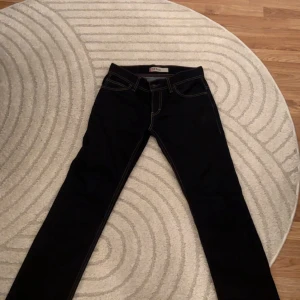 Levi's 511 mörkblå jeansbyxor W32 L32 - Säljer ett par mörkblå Levi's 511 jeans med klassisk femficksdesign och kontrastsömmar. Byxorna har slim passform och raka ben, perfekt för en stilren look. Ikonisk läderpatch bak i midjan och snygga detaljer.