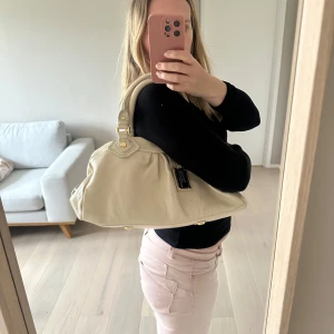 Cremevit Classic Q groove Marc Jacobs väska - Säljer sommarväskan nr 1 - en snygg krämvit handväska från Marc Jacobs (Classic Q Groove) med guldiga metalldetaljer och dubbla handtag. Väskan har en avtagbar axelrem och dragkedja upptill. Insidan är fodrad med mönstrat tyg. Perfekt för dig som vill ha en stilren och klassisk accessoar. Den större modellen. Mått 37 cm lång x 20 cm hög. Duatbag. Så populär och svår att få tag på. Ser knappt använd ut! 