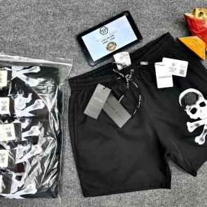 Svarta shorts med dödskalle från Philipp Plein - Svarta shorts från Philipp Plein med vit dödskalle- och korsben-tryck på ena benet samt metallbadge. Elastisk midja med snörning och logotypdetaljer på snörena. Perfekta för en edgy streetstil. Storlek S.M.L.XL 