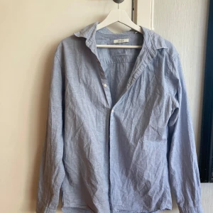 Ljusblå skjorta från Jack & Jones - En klassisk ljusblå skjorta från Jack & Jones med lång ärm och knappar framtill. Skjortan har en avslappnad passform och är tillverkad i ett mjukt bomullsmaterial. Perfekt till jeans eller chinos.