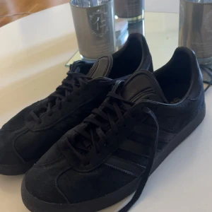 Svarta Adidas Campus sneakers i mocka - Säljer ett par svarta Adidas Campus sneakers i mocka. Klassisk design med svarta ränder på sidorna och snörning framtill. Perfekta för dig som gillar stilrena och tidlösa skor. Inga större defekter på dem