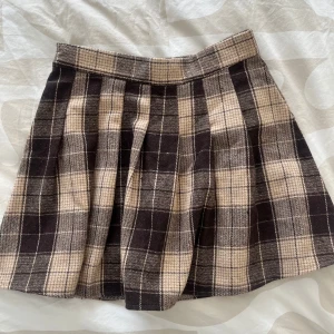 Rutig kortkjol i beige och brun - Säljer en superfin kortkjol med rutigt mönster i beige och brunt. Kjolen har bred linning och veckad design som ger en snygg siluett. Perfekt att styla med en enkel topp eller stickad tröja. Lite tjockare tyg! Passar vår, sommar och höst!