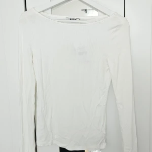 Vit ribbad långärmad topp från NA-KD - Säljer en enkel och stilren vit långärmad topp från NA-KD. Toppen är ribbad och har en rundad halsringning. Perfekt att matcha med jeans eller kjol för en clean look.