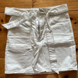 Vit jeanskjol från Gina  - Säljer en vit jeanskjol från Gina Tricot  i storlek 38. Kjolen har två stora fickor fram, två bakfickor och ett matchande bälte i midjan. Klassisk rak modell som är enkel att styla till olika looks.