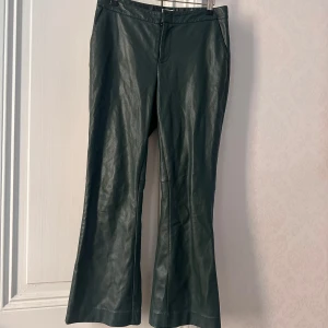 Mörkgröna skinnbyxor från Twist - Snygga mörkgröna skinnbyxor från Twist med klassisk passform och lätt utsvängda ben. Byxorna har dragkedja framtill och är perfekta för dig som vill ha en cool och trendig look. Byxorna är i modellen som är lite kortare så på mig som är 159 så slutar de ungefär 10cm från fötterna💗