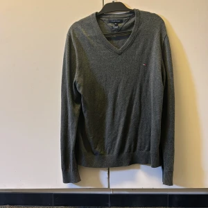 Grå v-ringad tröja från Tommy Hilfiger - Mörkgrå v-ringad tröja från Tommy Hilfiger med liten broderad logga på bröstet. Tröjan är i mjuk bomull och har långa ärmar samt ribbade muddar vid ärmslut och nederkant. Perfekt för lager-på-lager och stilren look. Nypris runt 1100 kr, mitt pris 199! Pris går att diskuteras! Hör av er vid minsta lilla fundering🤗
