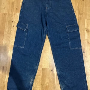 Blå cargobyxor från Sweet Sktsbs - Säljer ett par mörkblå cargobyxor från Sweet Sktsbs med stora fickor på sidorna och raka ben. Byxorna har klassisk jeanslook och är perfekta för en avslappnad streetstil.