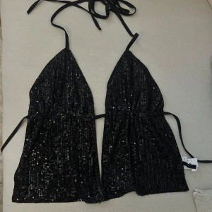 Svart glittrig festtopp - Säljer en svart snygg glittrig festtopp med öppen rygg som man knyter, endast använd en gång på nyår så den är i väldigt fint skick!!