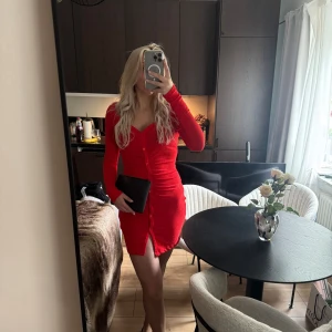 Röd klänning med knappar - Säljer en snygg röd omlottklänning med långa ärmar och knappar framtill. Klänningen har en v-ringad halsringning och är kort i modellen. Från Nakd och helt slutsåld får så fin passform!❤️