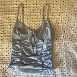 Ljusblå croppad linnetopp med knyt - Säljer en ljusblå croppad linnetopp med smala axelband och v-ringning. Toppen har rynkade sidor, knyt fram och vågig kant nertill. Toppen har använts en del men är fortfarande i mycket bra skick.