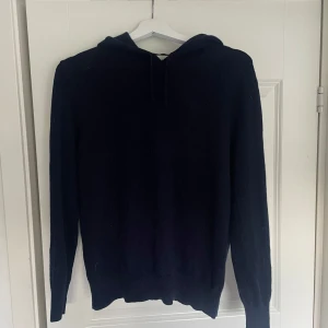 Marinblå stickad hoodie - Marinblå Sayless stickad hoodie med huva och långa ärmar. Perfekt för kyliga dagar och enkel att matcha med det mesta. Klassisk modell utan synliga detaljer eller mönster. Nypris - 1000kr