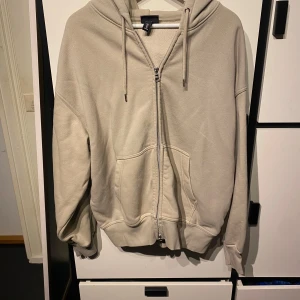 Beige oversized hoodie från H&M - Säljer en beige oversized hoodie från H&M med dragkedja framtill och stora fickor. Tröjan har huva med dragsko och långa ärmar. Perfekt för en avslappnad stil.