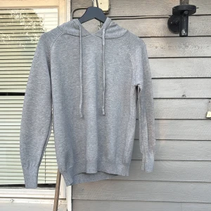 Grå hoodie med snören - Säljer nu min helt nya och oanvända, enkla och stilrena gråa hoodie med huva och snören. Tröjan har ribbade muddar vid ärmslut och nederkant. Riktigt skönt och töjbart material. Säljer p.g.a att det är för liten