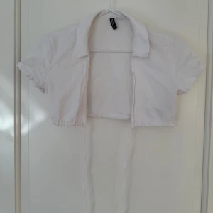 Vit croppad skjorta från hm - Säljer en vit croppad skjorta från hm med korta ärmar och klassisk krage. Skjortan har knytband framtill och är tillverkad i 100% bomull. Perfekt för en trendig och avslappnad stil.