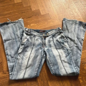 Blå lågmidjade bootcut jeans  -  blå vintage lågmidjade bootcut jeans med markerade sömmar framtill och slitna, råa benslut. Storlek S 