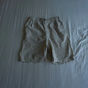 Beige linneshorts från H&M - Säljer ett par ljusbeige shorts från H&M i luftig linnemix. De har elastisk midja med knapp, fickor på sidorna och avslappnad passform. Perfekta för varma dagar och enkel stil.