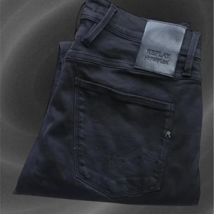 Svarta Replay Hyperflex jeansbyxor - Säljer ett par svarta Replay Hyperflex jeansbyxor i modellen Anbass. Byxorna har klassisk femficksdesign, silverfärgade knappar och logotypdetaljer vid fickorna. Stretchigt material för extra komfort och snygg passform. Kom med frågor!