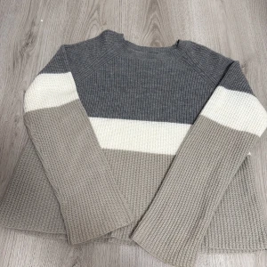 Randig stickad tröja från SHEIN - Mysig stickad tröja från SHEIN med breda ränder i grått, beige och vitt. Tröjan har lång ärm, rund halsringning och en relaxed passform. Väldigt mysig och inte för tjock