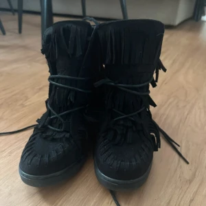 Fransskor - Säljer ett par svarta boots med fransar och snörning framtill. Skorna har en platt sula och är tillverkade i mocka. Perfekta för dig som vill sticka ut med en cool och bohemisk stil. Perfekta som sommarskor! Jättesnygga!!💕