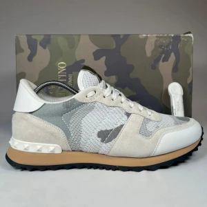 Valentino Rockrunner sneakers i grått och vitt - Säljer ett par Valentino Rockrunner sneakers i grått, vitt och beige med kamouflagemönster. Skorna har snörning, rund tå och detaljer i mocka, skinn och textil. Snygg gummisula med nitar på hälen och klassisk Valentino-logga på plösen.