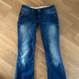 Blå bootcut jeans lågmidjade y2k - Snygga blå jeans från Mavi med bootcut passform och klassisk femficksdesign. Jeansen har slitningar framtill och bakfickor med dekorativa sömmar. Perfekta för en avslappnad stil. Syd extra Lågmidjade och uppsydda nertill, passar 165-170cm