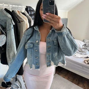  jeansjacka  - Trendig jeansjacka i ljusblå denim med råa, fransiga kanter nertill. Klassisk krage, två bröstfickor med lock och knappar framtill. Perfekt för att lyfta en enkel outfit.