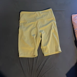 Gröna cykelshorts från H&M Sport - Säljer ett par gröna cykelshorts från H&M Sport med hög midja. De är tillverkade i ett stretchigt syntetmaterial och har en tight passform som passar perfekt för träning eller vardagsaktiviteter.