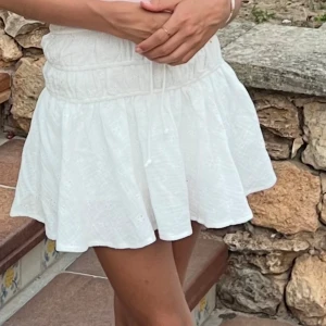 Vit kortkjol från Sky to Moon! - Supersöt vit kortkjol från Sky to Moon med broderade detaljer och smock i midjan. Kjolen har en volangig och luftig passform med knytband i midjan. Använd 1gång