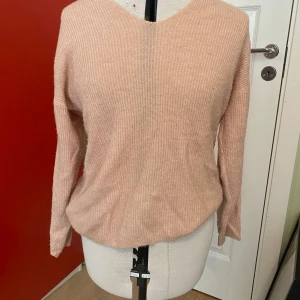 Rosa stickad tröja vero Moda - Mysig rosa ribbad tröja från vero Moda  med v-ringad hals och långa ärmar. Perfekt för lager-på-lager och enkel att matcha med olika outfits. Materialet är mjukt och stretchigt för extra komfort.