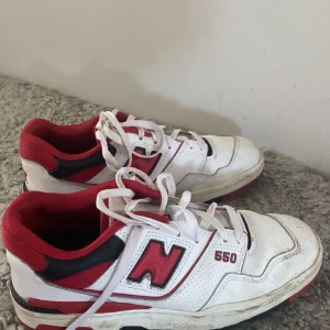 Vita och röda New Balance 550 sneakers - Säljer ett par New Balance 550 sneakers i vitt med röda och svarta detaljer. Skorna har snörning och en klassisk retrodesign med rund tå och platt sula. Perfekta för dig som gillar streetwear och sportig stil.
