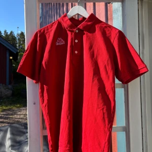 Röd pikétröja från Kappa - Snygg röd pikétröja från Kappa med klassisk krage och tre knappar framtill. Kappa-logga broderad på bröstet. Perfekt för en sportig och avslappnad stil.