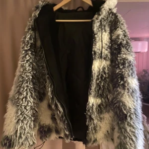 Gråvit pälsjacka med huva - Säljer en fluffig och trendig pälsjacka i grått och vitt med huva och dragkedja. Fodrad insida. Köpt i London för 1500. Använd men i bra skick.