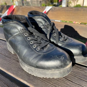Svarta boots med ormmönstrad detalj - Säljer ett par svarta boots med snörning och cool ormmönstrad detalj runt skaftet. Skorna har robust platt sula och är tillverkade i skinnliknande material. Perfekta för dig som vill ha en edgy look till vardags.