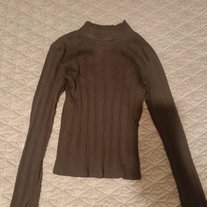 Brun ribbad polotröja - Säljer en brun ribbad polotröja med lång ärm. Tröjan har en tight passform och är tillverkad i ett stretchigt material som sitter snyggt på kroppen. Perfekt att styla med jeans eller kjol.