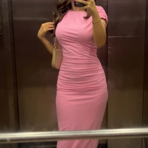 Rosa tight långklänning - Säljer en snygg rosa långklänning med tight passform och korta ärmar. Klänningen har en enkel och stilren design som framhäver figuren. Perfekt för dig som gillar en feminin och modern look.