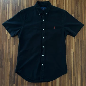 Svart kortärmad skjorta från Ralph Lauren - Svart Ralph Lauren skjorta   |  Skick 7/10 |  Size S |  Slim fit  |  Bredd 44,5 cm Längd 70 cm  |  Perfekt för en stilren look till sommaren.  Hör av dig vid minsta fråga eller fundering :)