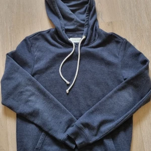 Mörkgrå hoodie från Pier One - Mysig mörkgrå hoodie från Pier One med justerbar huva och vita snören. Tröjan har långa ärmar och en klassisk passform, perfekt för en avslappnad stil.
