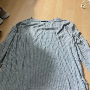 Grå ribbad långärmad tröja från 157 - Säljer en enkel och stilren grå ribbad långärmad tröja från 157. Perfekt basplagg med rund halsringning och mjukt material. Passar till det mesta och är superbekväm att bära.