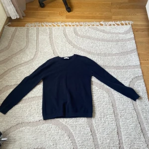 Mörkblå tröja från Tiger of Sweden - Säljer en stilren mörkblå tröja från Tiger of Sweden. Tröjan har rund halsringning och långa ärmar. Perfekt för dig som gillar klassisk och enkel stil och en old money look. Materialet känns mjukt och bekvämt.