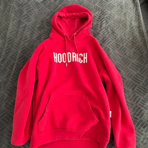 Röd hoodie från Hoodrich - Säljer en röd hoodie från Hoodrich med vit logga på bröstet. Tröjan har huva med dragsko och en stor magficka framtill. Perfekt för dig som gillar streetwear och vill sticka ut med färg.